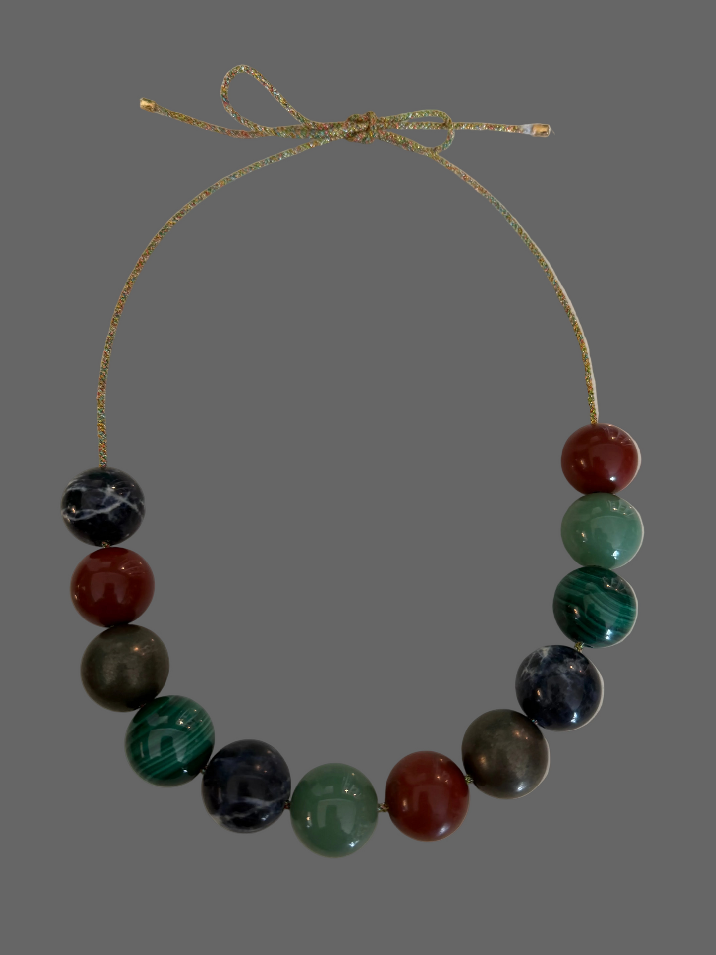 A beaded necklace with multicolored polished round beads on a thin adjustable cord, photographed on a plain light surface.