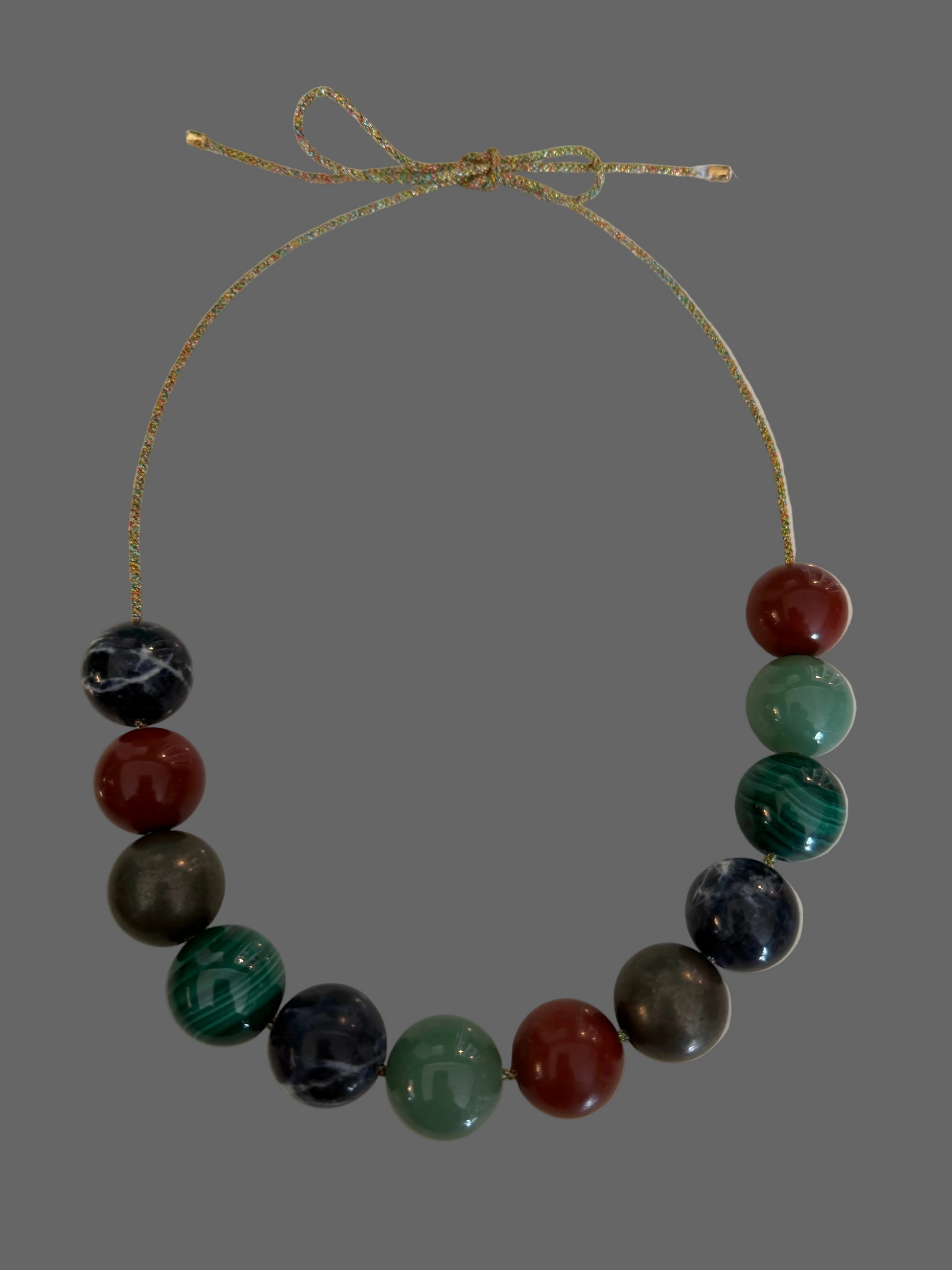 A beaded necklace with multicolored polished round beads on a thin adjustable cord, photographed on a plain light surface.